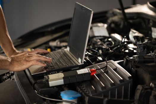 Computer diagnostics of the car. European car mechanic holds a digital device. Auto mechanic uses laptop while conducting diagnostics test. Modern car service.
