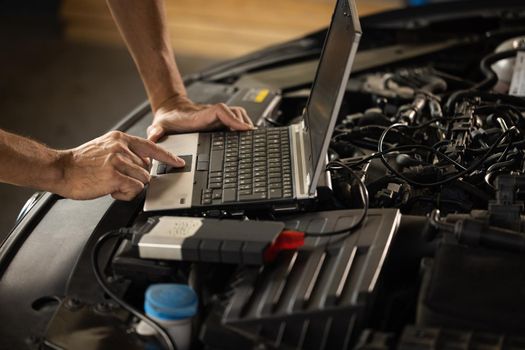 Specialist inspecting the vehicle in order to find broken components and errors in data logs. Automobile service, car mechanic. Auto mechanic uses a laptop while conducting diagnostics test.