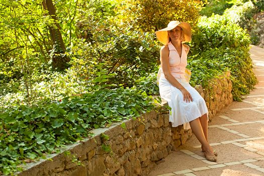 Beautiful caucasian woman in white dress sitting in summer park