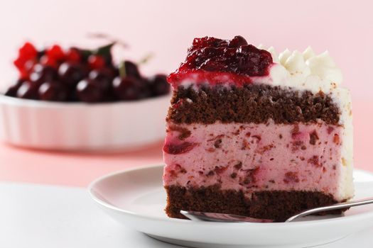 A piece of biscuit cake, with cherry souffl with cream cheese and cherry confiture on a pink and white background. close-up