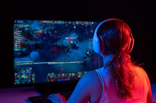 Rear view of a caucasian woman playing a computer game in neon light in the dark