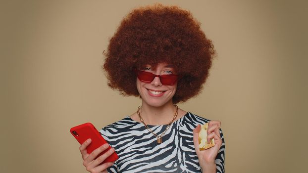 Happy young woman use smartphone, plastic credit bank card, browsing say wow yes, found out great big win, success lotter, good news, purchases online shopping. Adult girl on beige studio background