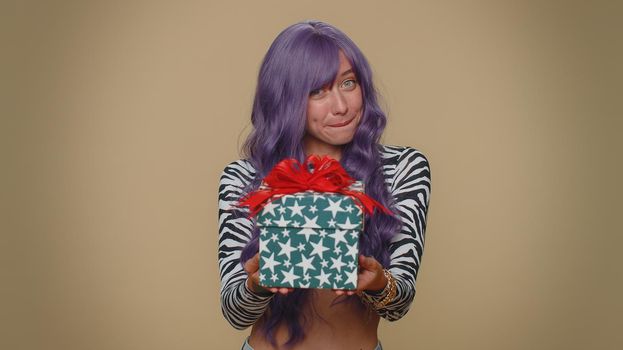 Positive smiling lovely pretty young woman presenting birthday gift box stretches out hands, offer wrapped present career bonus, celebrating party. Adult stylish girl on beige studio background indoor