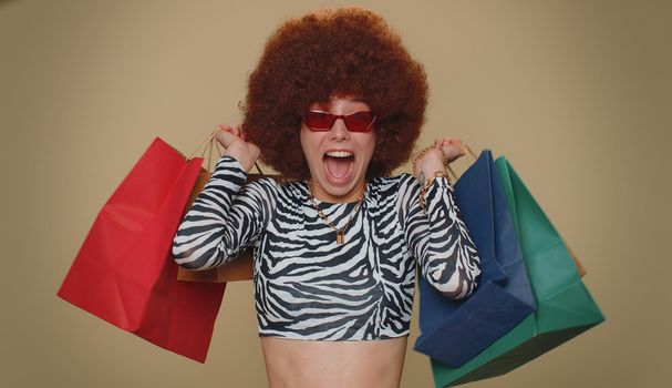 Happy young woman showing shopping bags, advertising discounts, smiling looking amazed with low prices, shopping on Black Friday holidays . Adult stylish girl isolated alone on beige studio background