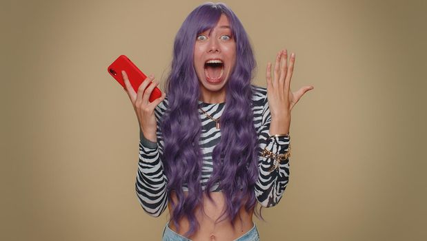 Happy excited joyful young woman use smartphone typing browsing say wow yes, found out great big win news doing winner gesture. Adult stylish female girl isolated on beige studio background indoors