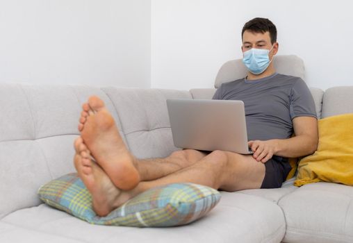 young man in mask and with laptop sitting on sofa. High quality photo