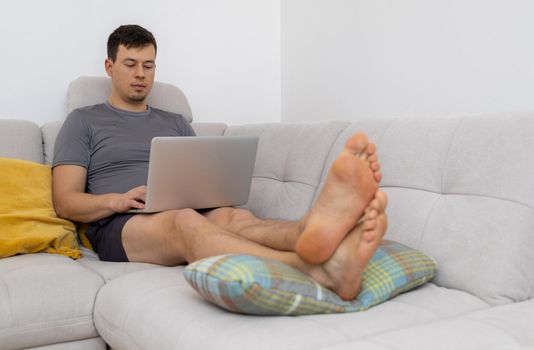 young man with laptop sitting on sofa with legs. High quality photo