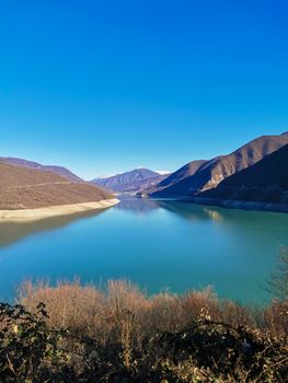 The Ananuri River is country of Georgia surrounded by mountains. Amazing view mountain lake on sunny winter day. Snowy peaks of mountains against the background of water. Gorgeous nature landscape