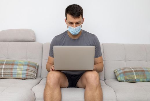 young man in mask and with laptop sitting on sofa. High quality photo