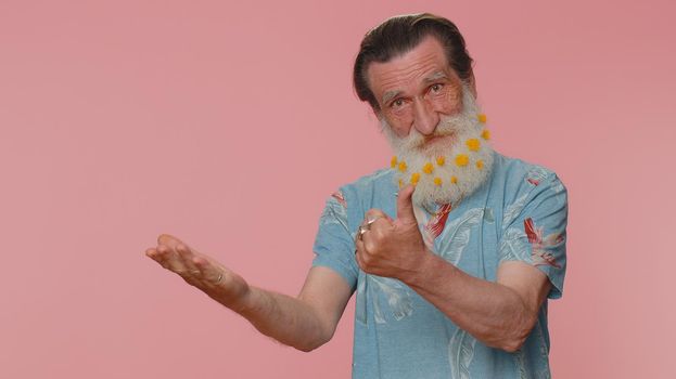 Handsome senior man showing thumbs up and pointing empty place, advertising area for commercial text, copy space for goods promotion. Elderly grandfather. Studio shot indoors on pink wall background