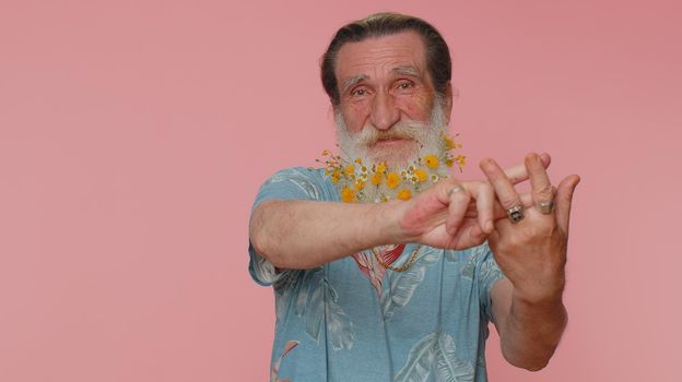 Cheerful senior man with flowers in beard showing hashtag symbol with hands, likes tagged message, popular viral content, sign to follow internet online trends. Elderly grandfather on pink studio wall