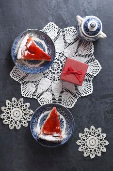 Christmas red strawberry pie on blue plates and a gift in a red box on the table, flat lay colorful food on white knitted napkins in the form of snowflakes, winter mood. High quality photo
