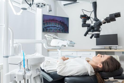 Female dentist using dental microscope treating patient teeth at dental clinic office. Medicine, dentistry and health care concept