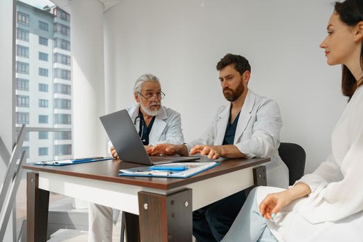 Two doctors in white uniform consult female patient at meeting in private clinic. High quality photo