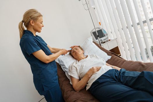 Doctor measures patient's temperature with non-contact thermometer during treatment in hospital ward