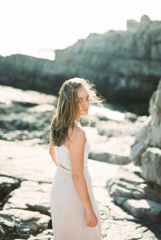 Young woman stands half-turned on a rock with her hair flying. High quality photo
