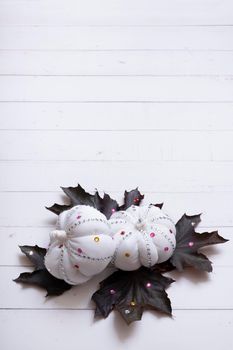 Creative autumn composition with white textile decorative pumpkins and dark maple leaves decorated rhinestones on wooden background. Vertical photo. Copy space.