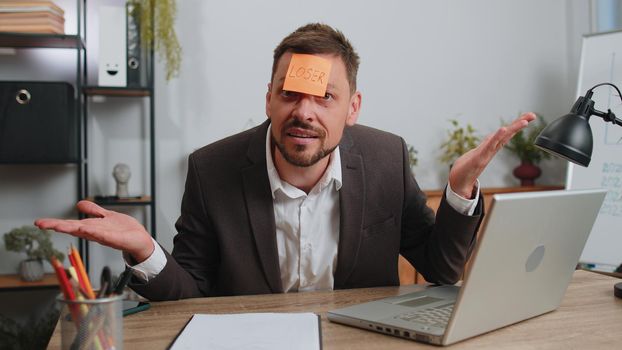 Businessman in suit with inscription note text Loser on forehead working on laptop loses becoming surprised sudden lottery results, bad news, fortune loss, fail at office. Male freelancer business man