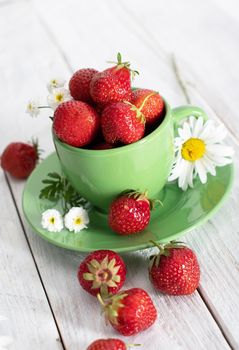 ripe strawberries from the garden in a green mug with white chamomile, fruity summer still life, close-up. High quality photo
