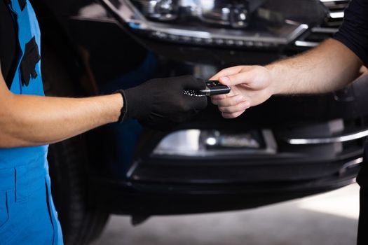 Close up shot of hands of mechanic giving car key to male client after servicing in auto repair shop. Vehicle breaks down. Car repair.