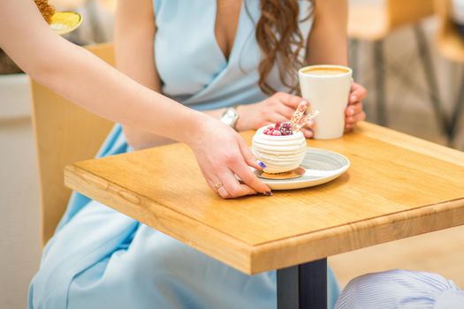 The waitress's hand puts the piece of cupcake on the table at a cafe, woman hand is putting round little pastry on the table on a background of a female in a blue dress
