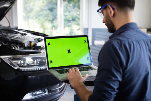 Car Service Mechanic is Running Diagnostics Software on an Advanced Computer with Green Screen Mock Up. Specialist Inspecting the Vehicle in Order to Find Broken Components and Errors in Data Logs.