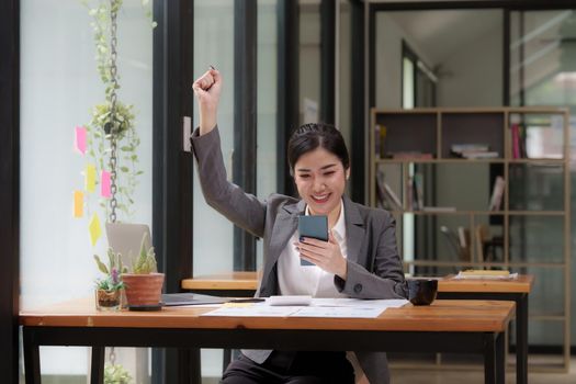 Happy Asian man using smartphone while have a good news working at office.