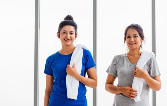 Asian adult and young woman smiling with towel around neck after yoga and exercise. Portrait of happy beautiful female standing indoor yoga studio, sport healthy workout concept