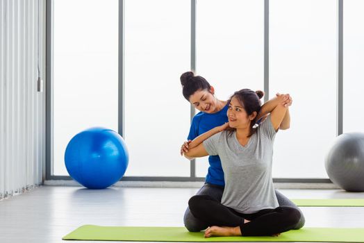 Asian young woman teacher teach adult student doing yoga stretching position in studio. Two woman teaching yoga and fun together, female sport fit workout concept