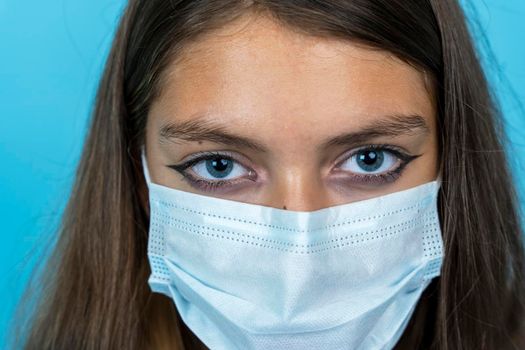 the face of a girl in a medical mask on a blue background. Portrait of a young woman in a medical face mask. Lifestyle related to COVID