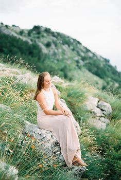 Smiling girl sitting on a stone in the mountains. High quality photo