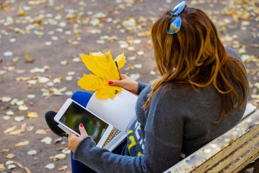 Close-up, the girl sits on a bench in the park and drinks coffee to take away. copy space.working remotely on a beautiful sunny autumn nature.
