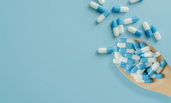 Top view of blue-white antibiotic capsule pills on wooden spoon and blue background. Antibiotic drug resistance. Prescription drug. Medical care. Pharmaceutical care. Antimicrobial drug overuse.