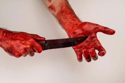 A man with bloody hands cuts himself with a knife