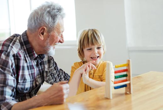 Portrait of grandfather and grandson having fun with an abacus tool or toy doing mathematic calculation and learning together at home