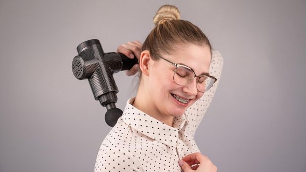 Smiling woman with braces uses a massager gun for her back