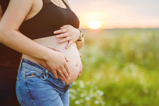 Man hugs a pregnant woman outdoors, at sunset