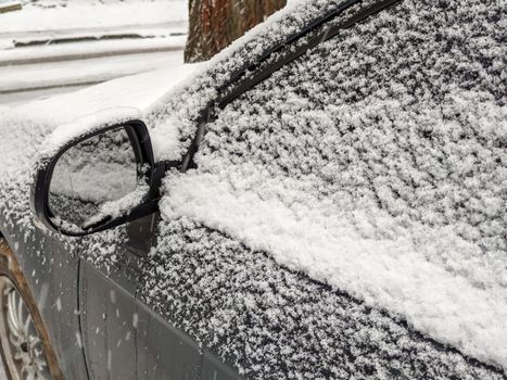 Left rear view mirror and side window of the car covered with snow.