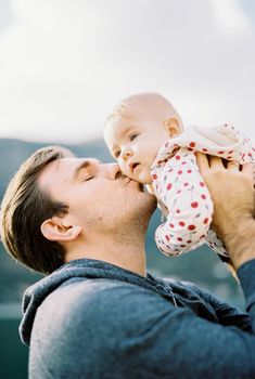 Dad lifts the baby above his head and kisses him on the cheek. Portrait. High quality photo