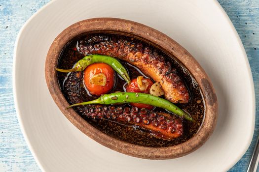 Casserole octopus with tomatoes and peppers on blue stone background