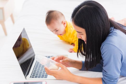 Asian new young beautiful mother finding and reads information on a laptop for milk mixing on a bottle in the bedroom at home