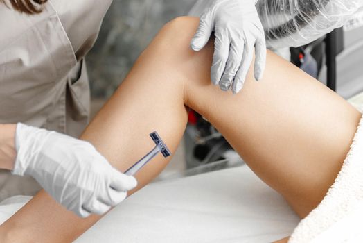A girl at a laser hair removal procedure shaves her legs before the procedure. Hair removal with a razor. Master shaves client's legs.