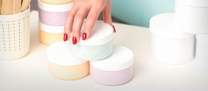 Beautician's hand takes jar with cosmetics from table offering and selling cosmetic products, moisturizing cream, wax paste