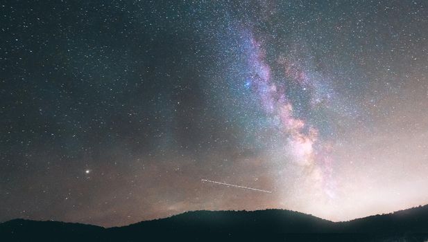 Night landscape with colorful Milky Way and yellow light at mountains. Starry sky with hills. Beautiful Universe.