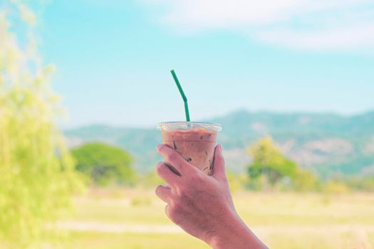 Hand hold iced latte coffee in a  tall glass. cold summer drink background