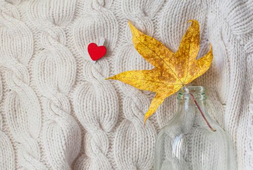 Hello autumn. Creative flat lay composition on light background. Yellow leaf, knitted sweater and small red heart. Copy space.