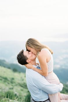 Man holds woman in his arms and kisses her standing high in the mountains. High quality photo