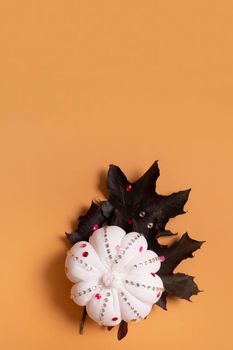 White decorative hand made pumpkin with shiny stones and maple leaves on colored background. Thanksgiving day concept