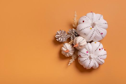 White decorative hand made pumpkins with shiny stones and pine cones on colored background. Thanksgiving day concept