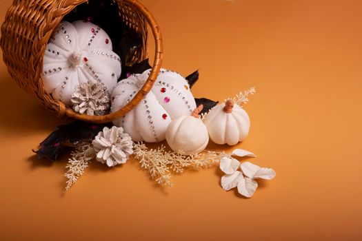 White decorative hand made pumpkins with shiny stones and pine cones in basket on colored background. Autumn harvest concept.